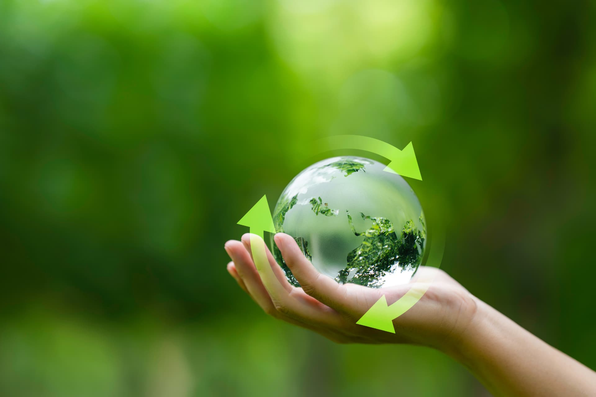 Hand holding a glass globe surrounded by green recycling arrows, representing environmental responsibility
